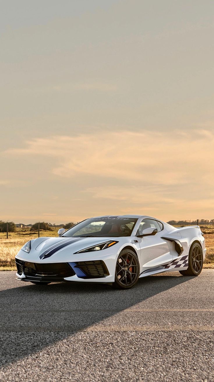 a white sports car parked on the side of the road in front of an open field