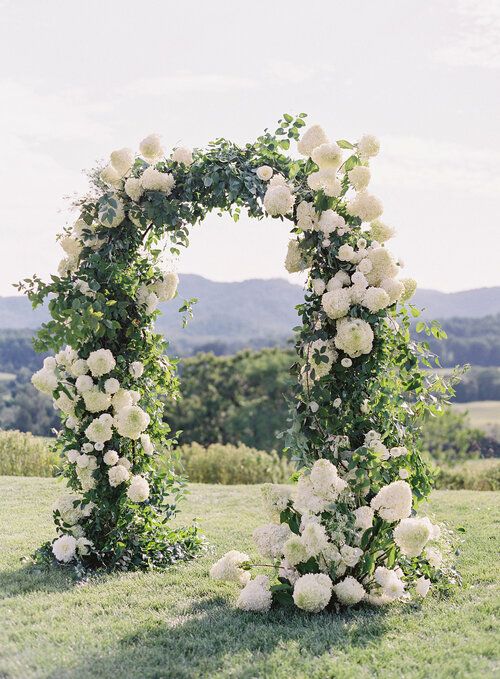 an outdoor wedding ceremony with white flowers and greenery on the grass in front of mountains