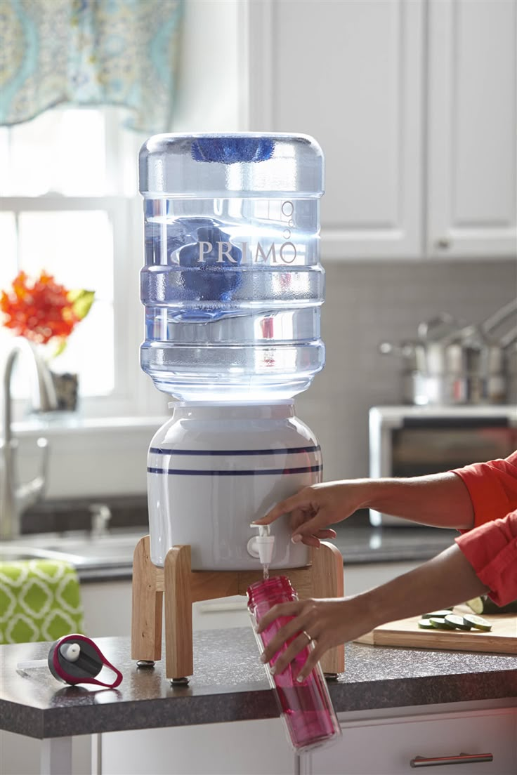 a woman is pouring water into a large container on top of a kitchen countertop