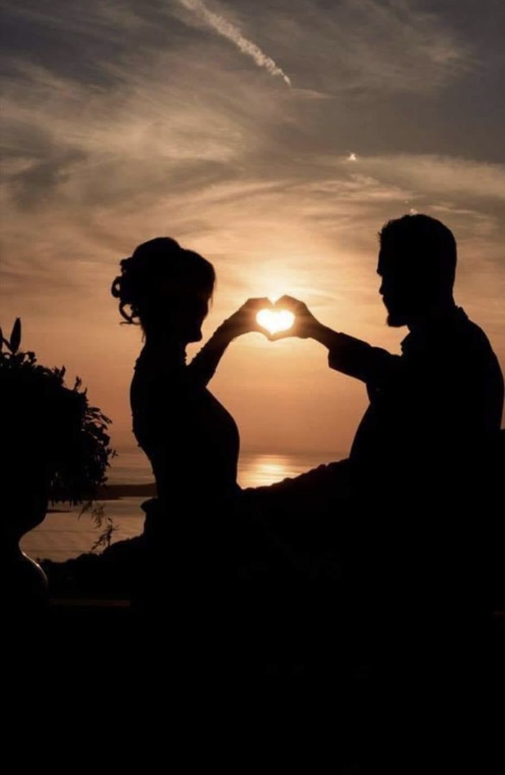 the silhouette of two people making a heart with their hands as the sun sets in the background