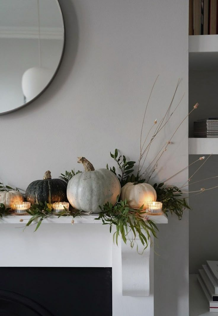 a mantle with candles, pumpkins and greenery in front of a round mirror