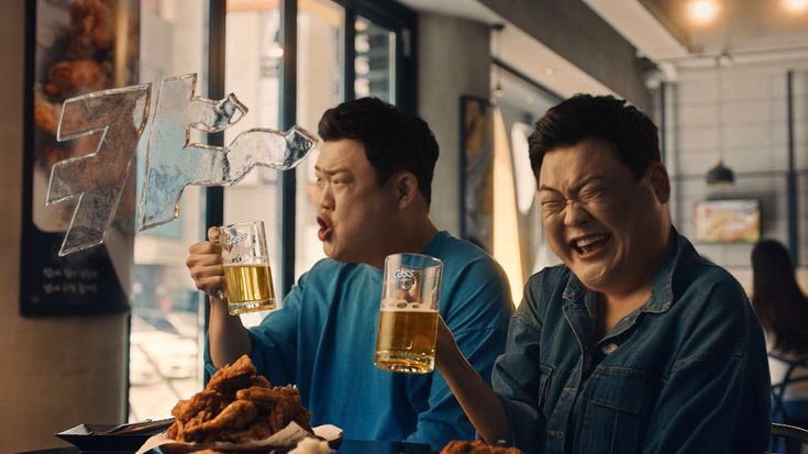 two men sitting at a table with beer glasses in their hands and food on the table