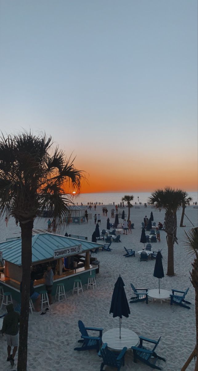 the beach is crowded with people and umbrellas at sunset or sunrise, while the sun sets