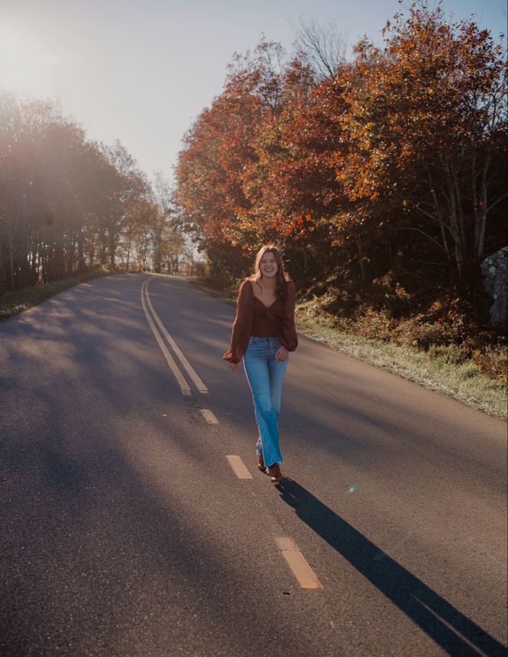 a woman walking down the middle of a road with trees in the backgroud