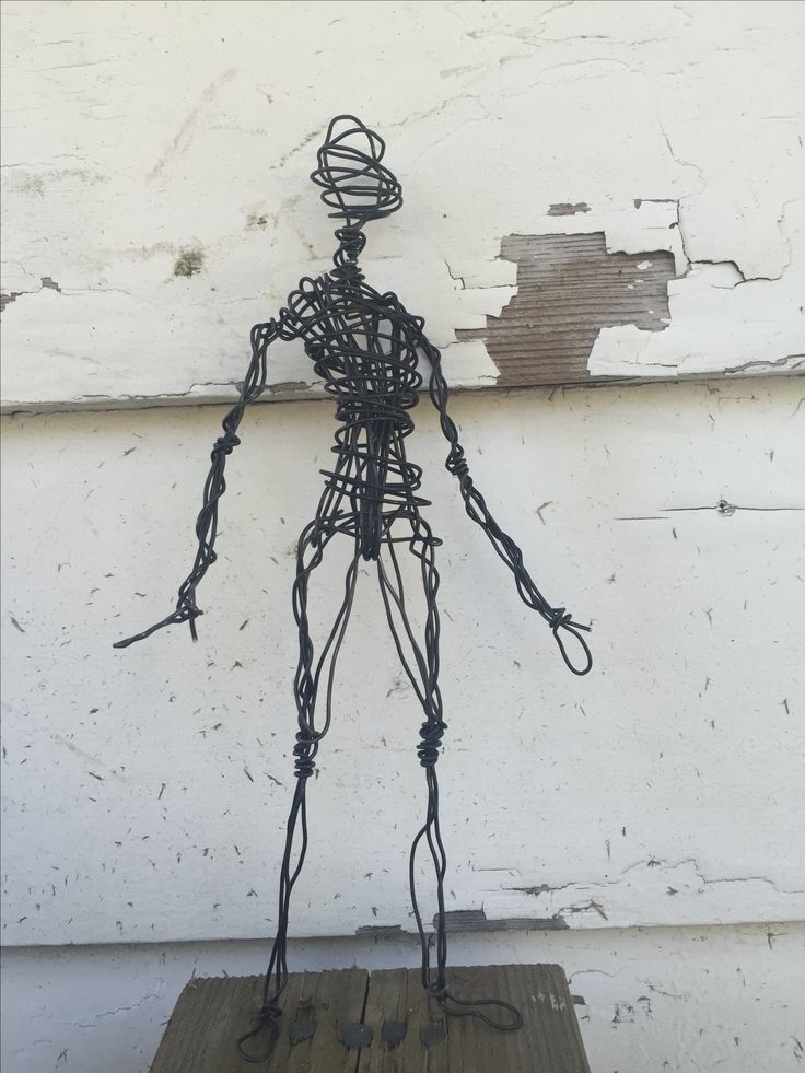 a wire man standing on top of a wooden table next to a white painted wall