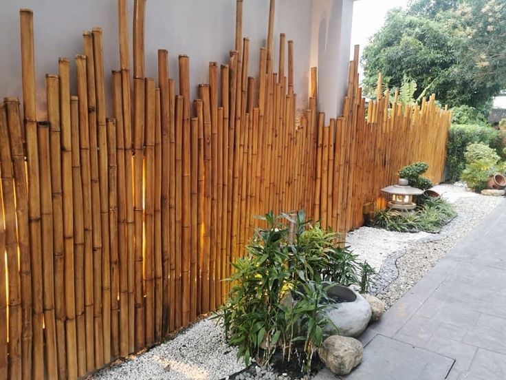 a bamboo fence with rocks and plants in the foreground, next to a walkway