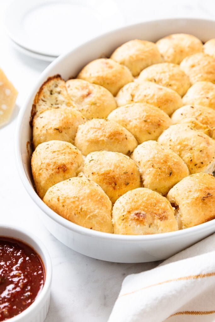 a casserole dish filled with rolls next to sauces and bread on a table