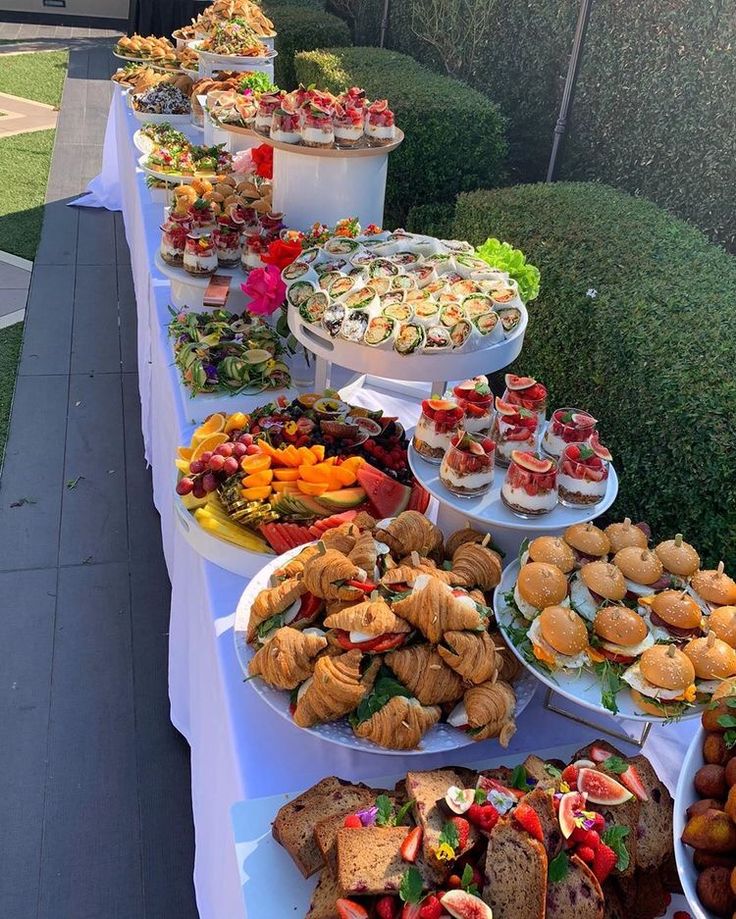 a long table filled with lots of food on top of a white tablecloth covered field