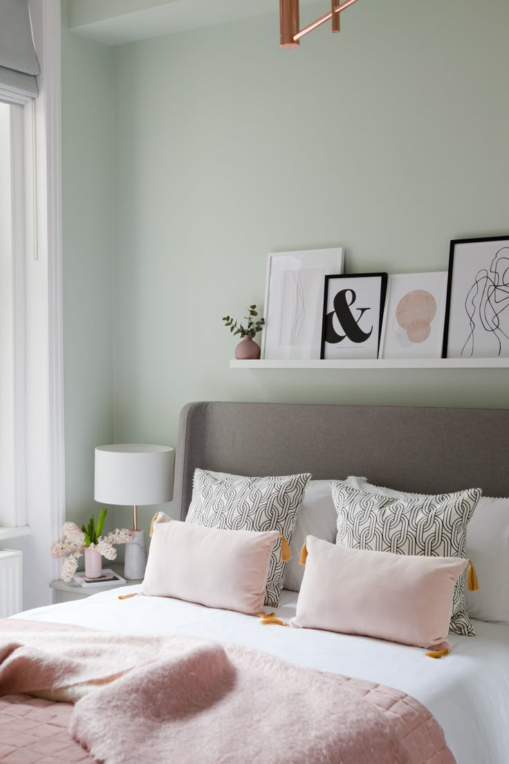 a bed with pink and white pillows on top of it in a bedroom next to a window