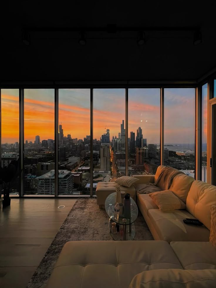 a living room filled with furniture and large windows overlooking the cityscape at sunset