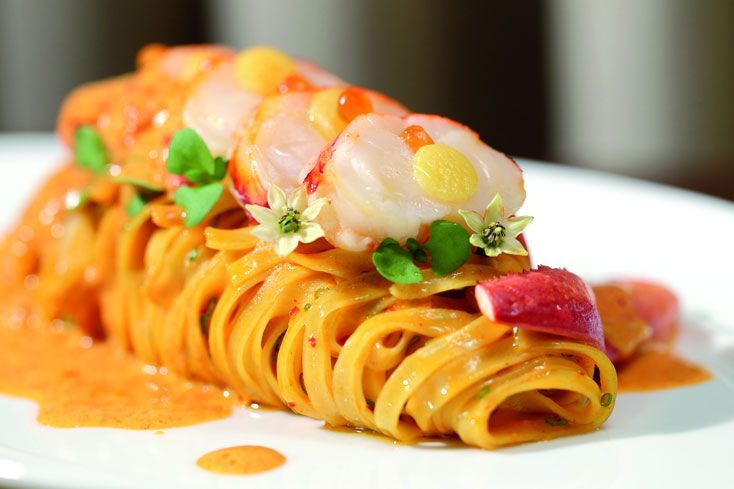 a pasta dish with shrimp and garnishes on the top, served on a white plate