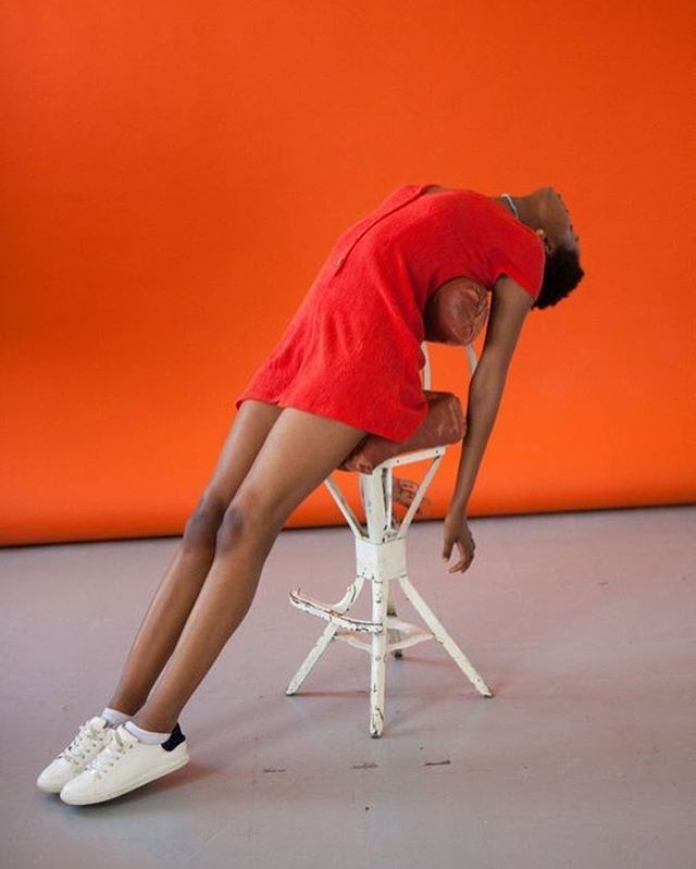 a woman in red shirt and white tennis shoes leaning on a chair with her head down