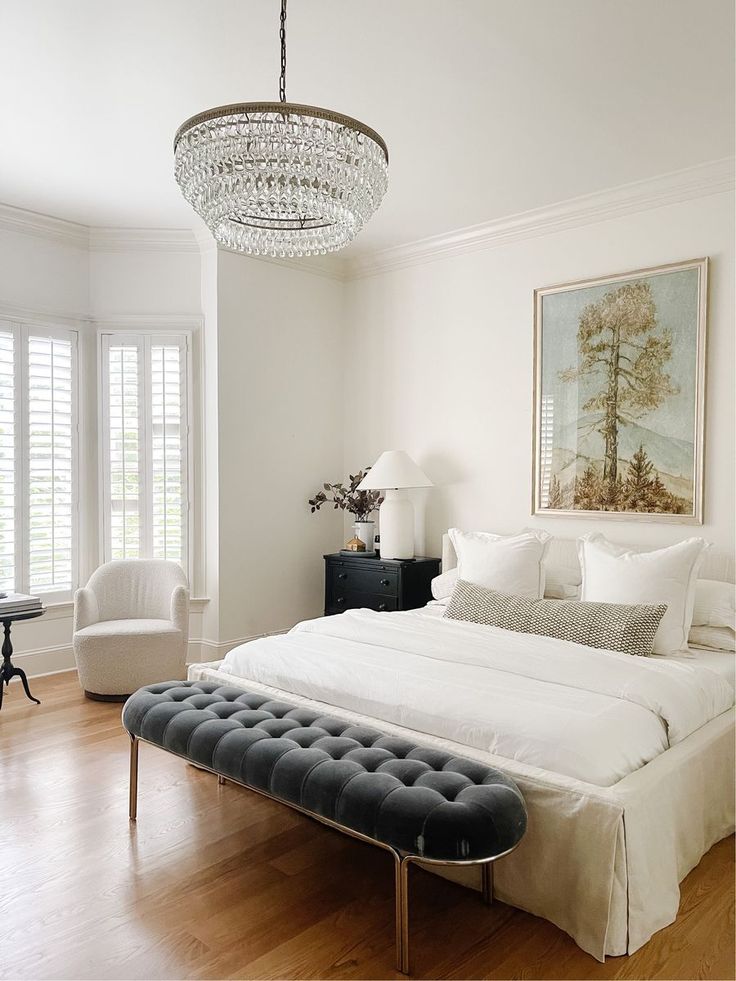 a bedroom with a bed, chair and chandelier hanging from the ceiling in front of two windows