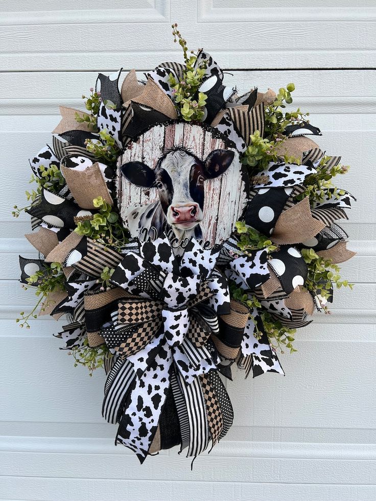 a cow head wreath hanging on the side of a garage door with black and white ribbons