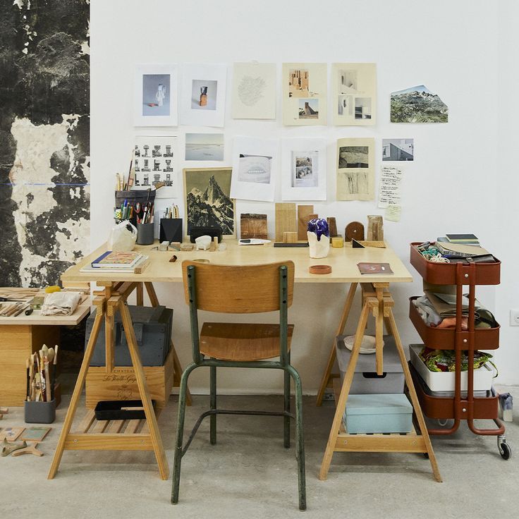 a desk with two chairs and many pictures on the wall behind it in an art studio