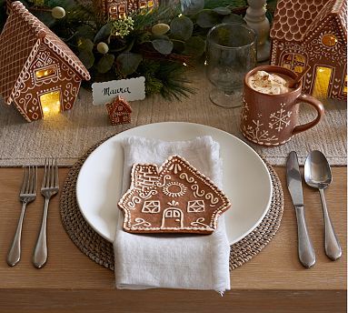 a table set for christmas with gingerbread house cookies on it and silverware in the foreground