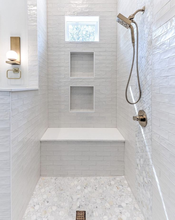 a walk in shower with white tile walls and flooring next to a shelf on the wall