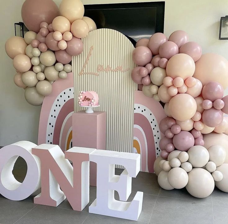 balloons are arranged around the word one in front of an arch with a pink and white theme