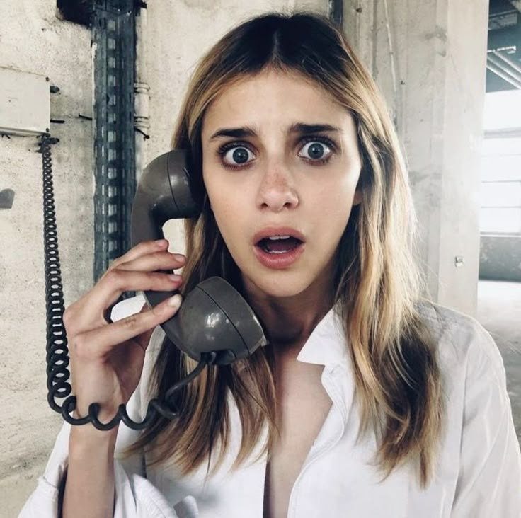 a woman holding an old phone up to her face and making a surprised face as she talks on the phone