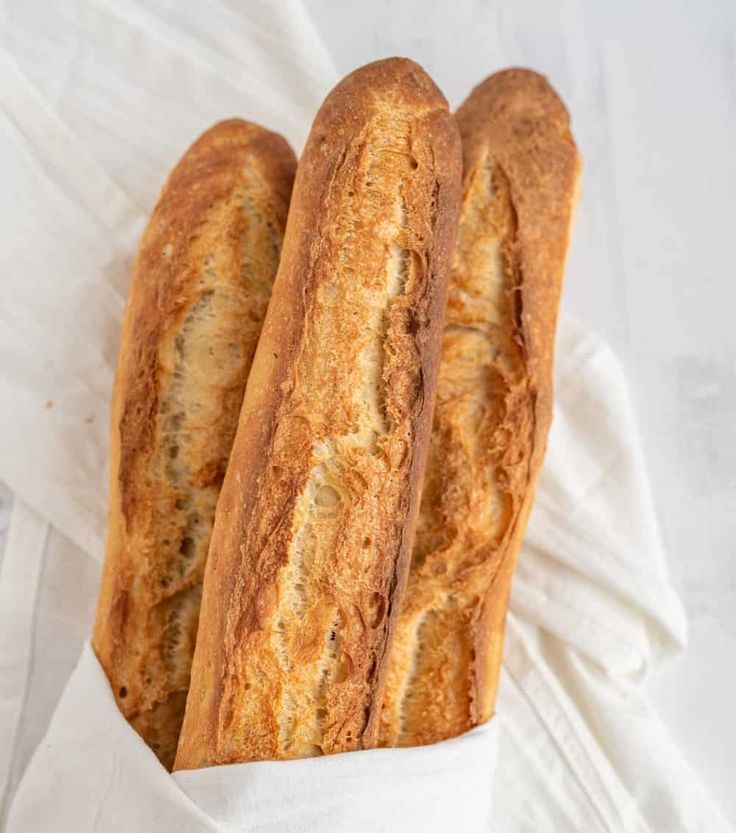 three loaves of bread sitting on top of a white cloth wrapped in wax paper