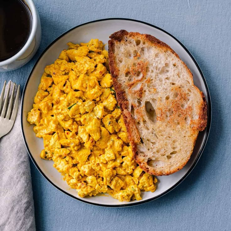 scrambled eggs and toast on a plate next to a cup of coffee