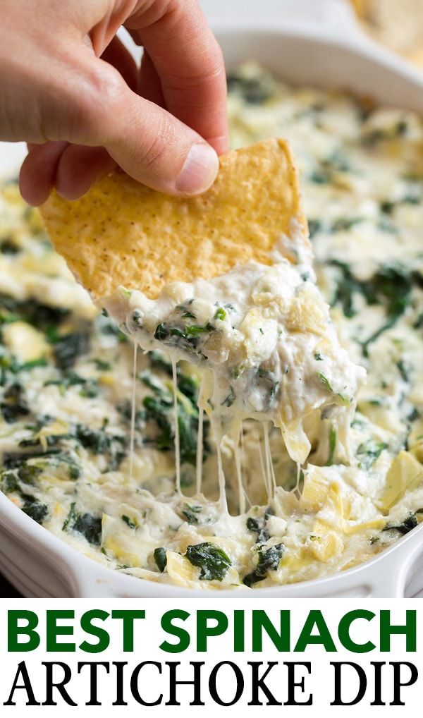 a hand dipping a tortilla chip into a bowl of spinach and cheese dip