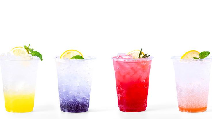 four different colored drinks with limes and lemon wedges on the rim, lined up in a row