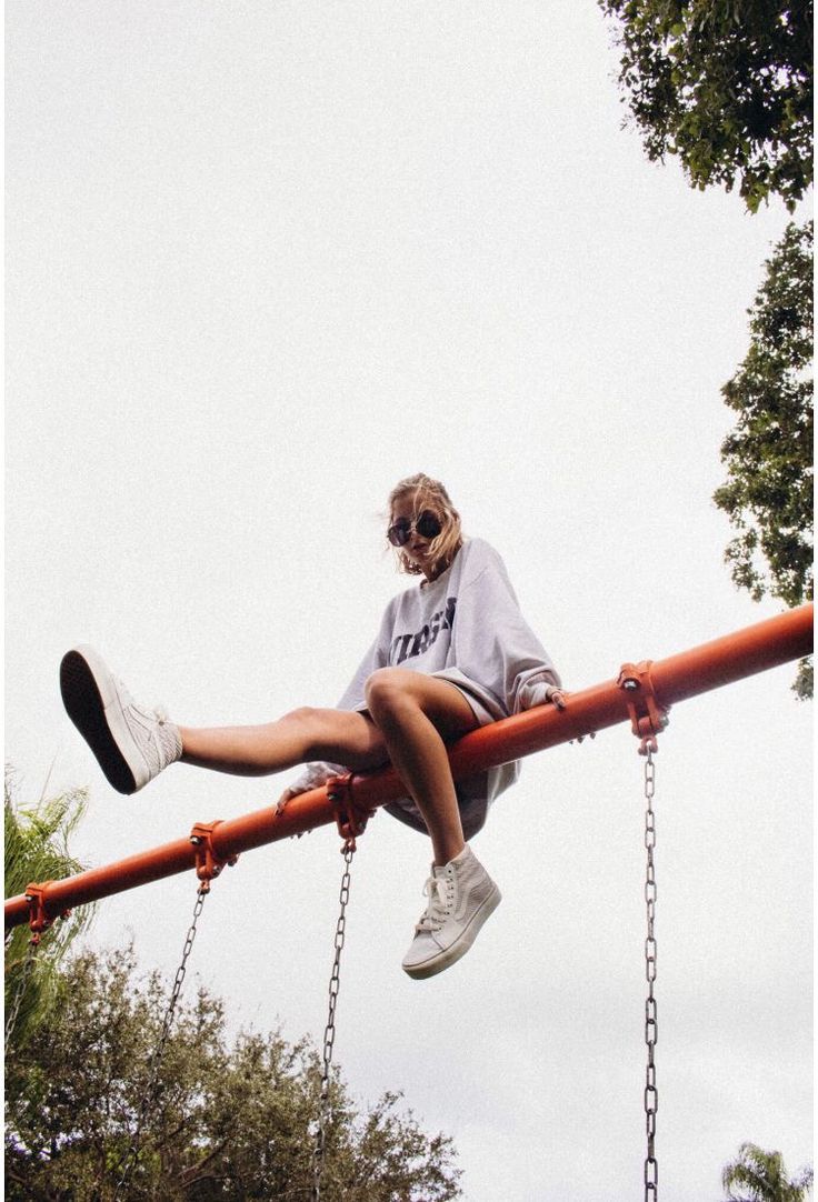 a woman sitting on top of a red metal pole with chains hanging from it's sides