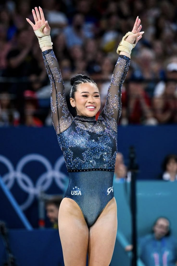 a woman in a blue leotard is holding her hands up and smiling at the camera