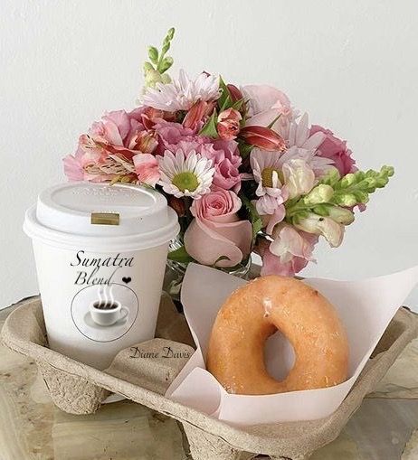 a cup of coffee, doughnut and flowers on a tray with a donut