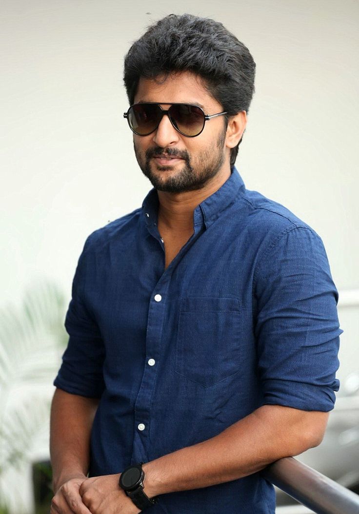 a man with sunglasses on standing next to a railing and looking at the camera while wearing a blue shirt