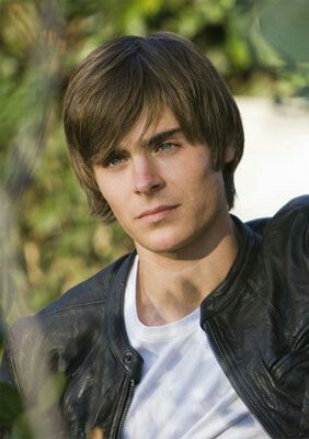 a young man wearing a black leather jacket and white t - shirt looking at the camera