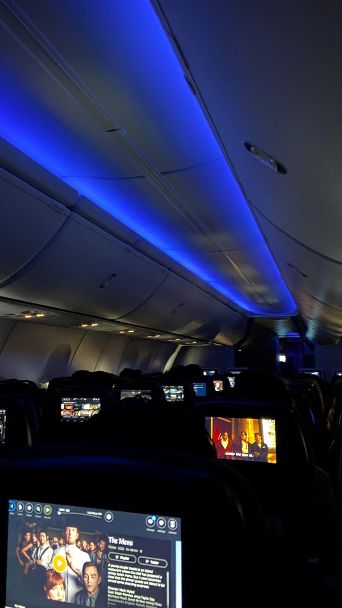 the interior of an airplane with blue lights on it and televisions in the aisle