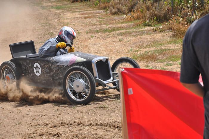 a man riding on the back of a black race car down a dirt road next to a red flag