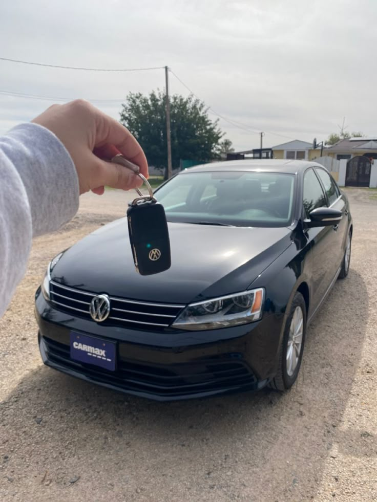 a person holding a car key in front of a black volkswagen