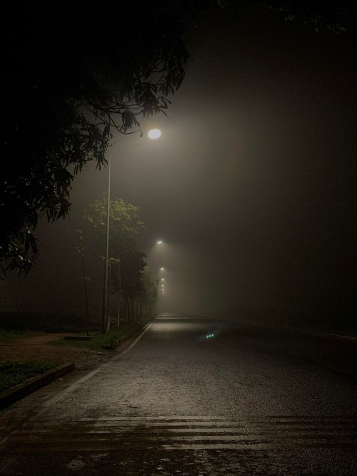 an empty street at night with the light on and fog in the air above it