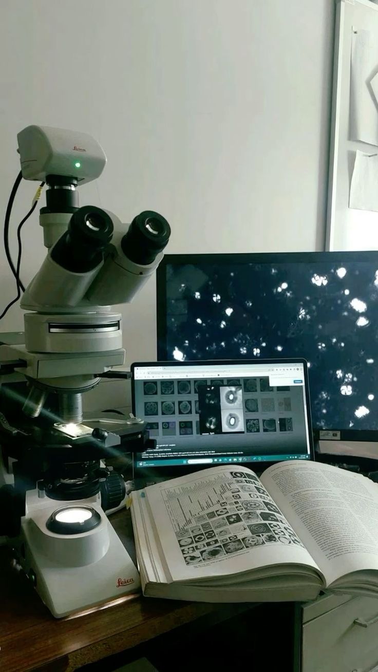 a laptop computer sitting on top of a desk next to a microscope and a book