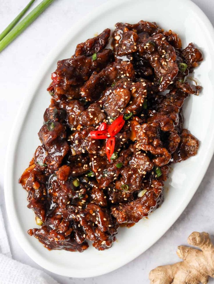 a white plate topped with meat covered in sauce and garnished with green onions