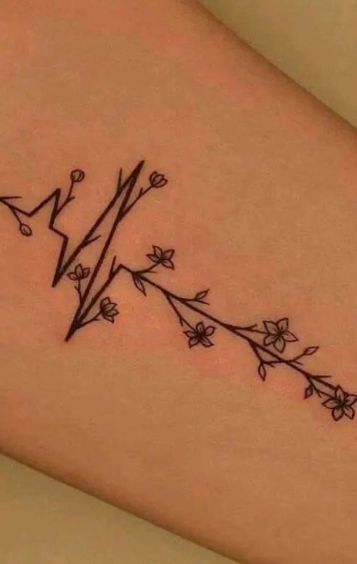 a small tattoo on the leg of a woman's arm with flowers and lightning bolt