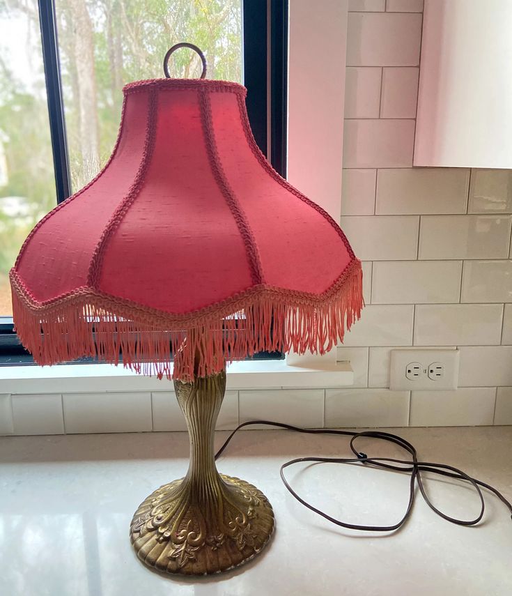 a pink lamp sitting on top of a white counter next to a window with a red shade