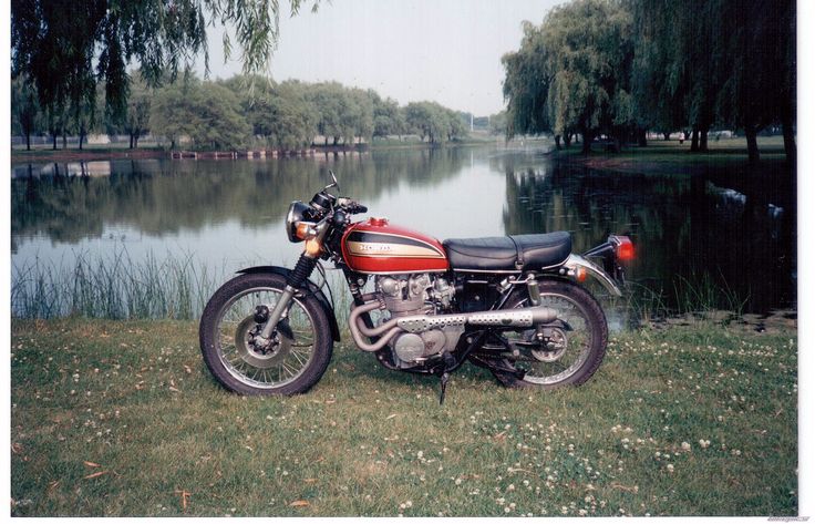 a red motorcycle parked next to a body of water on top of a lush green field