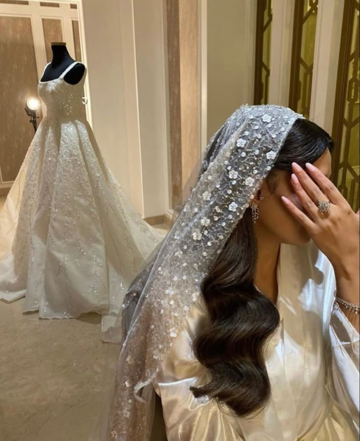 the bride is covering her face in front of wedding gowns on mannequins