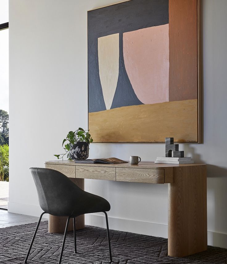 a desk with a painting on the wall above it and a chair in front of it