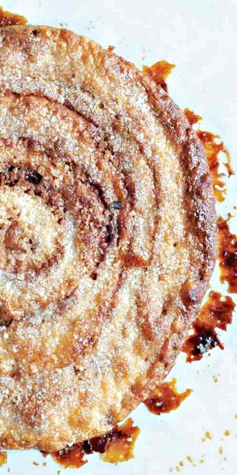 a cinnamon roll on a white plate covered in powdered sugar and brown syrups