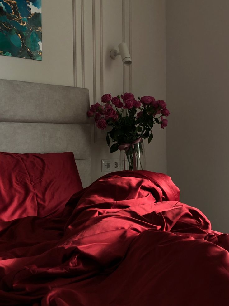 a vase filled with pink roses sitting on top of a bed covered in red sheets