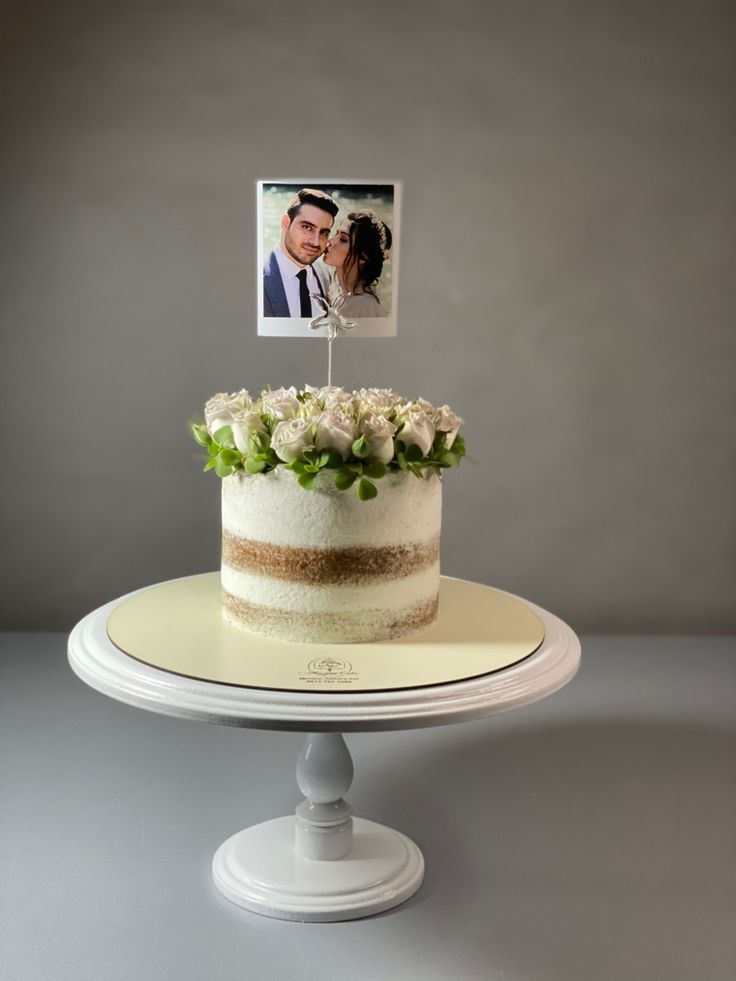 a wedding cake with a photo on top and flowers in the foreground, sitting on a white pedestal