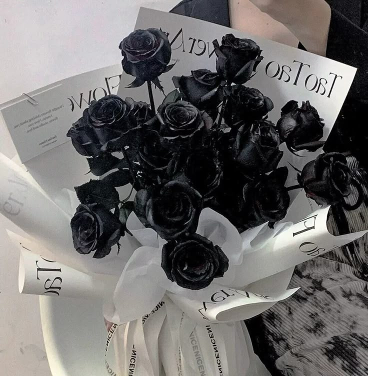 a bouquet of black roses sitting on top of a white plate with paper in it