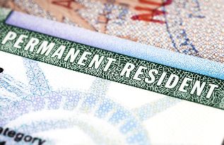 a green and white permit sitting on top of a pile of paper money with the word permanent resident printed on it