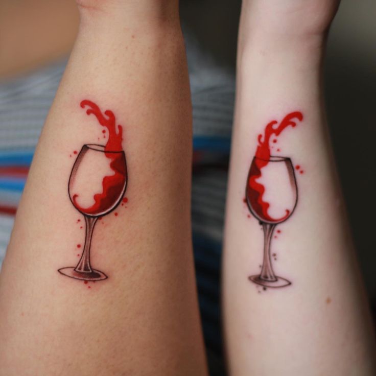 two people with matching tattoos on their arms holding wine glasses and red liquid pouring out of them