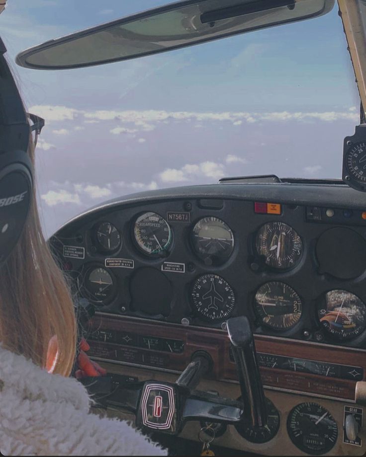 a woman sitting in the cockpit of an airplane looking out at the clouds and sky